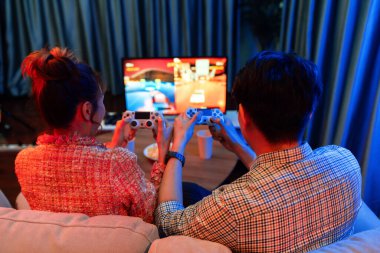 Kontrollü joystickli birkaç oyuncu, televizyon ekranında birlikte araba yarışı oyunu oynuyorlar. Arka tarafta atıştırmalıklar, modern konforlu evinde neon ışıklı oturma odasında kanepe. İnfobahn.