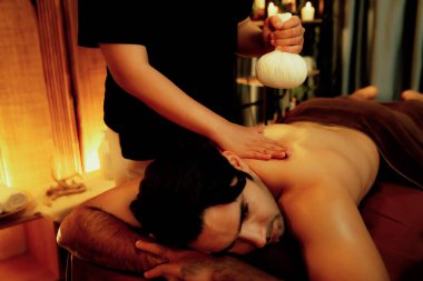 Sıcak bitkisel top spa masaj vücut tedavisi, masör erkek vücuduna nazikçe şifalı bitki torbası bastırıyor. Aromaterapi tesisinin sakinliği ve dinginliği kaplıca salonundaki mumların sıcacık ışığında. Sessiz.
