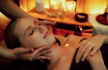 Beyaz kadın stres önleyici kafa masajı yapmaktan ve lüks otel veya otelde sıcak mum ışığında yüz güzelliği eğlencesi yapmaktan zevk alıyor. Sessiz.