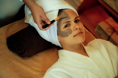 Kaplıca salonunun sakin atmosferi, kadın müşteri sıcak mum ve kömür kömürü yüz kremi masajıyla kendini yenileme zevkine kapılıyor. Yüz bakımı ve güzellik konsepti. Sessiz.