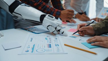 Bu resim, çağdaş bir ofisteki veri analizinde insanlarla işbirliği yapan bir robot kolu yakalar, yenilikçi çözümler için teknoloji ve takım çalışmasının karışımını vurgular. Noogenesis