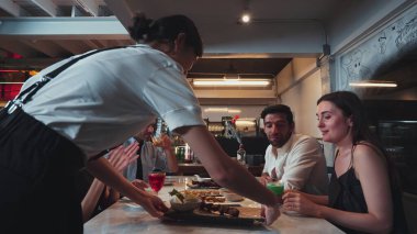 Grup arkadaşı ya da çift masada kokteyl içerken garson da lüks bir restoranda özel ızgara et menüsü sunuyor. Vinosity.