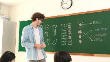 Öğrenciye bakarken, sınıfta matematik teorisi hakkında konuşan ve açıklayan beyaz bir öğretmen. Tahtanın önünde durup tahtaya işaret eden yetenekli bir eğitmen. Pedagoji.