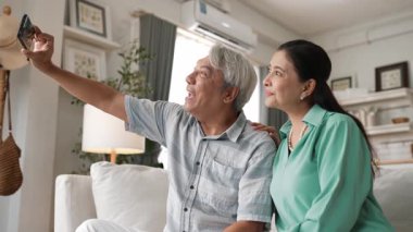 Mutlu büyükbaba ve büyükanneler evlerinde oğluyla görüntülü konuşma yapıyorlar. Yaşlı adam elinde akıllı bir telefonla kanepede otururken yaşlı kadın modern evde neşeli bir şekilde selamlıyor. Myrmidon.