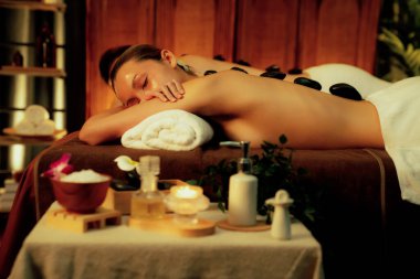 Sıcak mum ışığı olan lüks bir tatil köyündeki kaplıca salonunda sıcak taş masajı yapan mutlu çift, bazalt taşı masajının keyfini çıkarırken rahatlatıcı bir sıcaklıkla vücudun üzerinde süzülüyor. Sessiz.