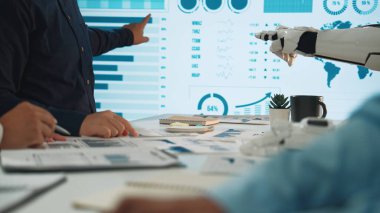 İş toplantısı sırasında iş birliği yapan insanlarla bir robotun dinamik bir sahnesi, profesyonel bir çevrede veri analizi ve teknolojik gelişimi vurguluyor. Noogenesis