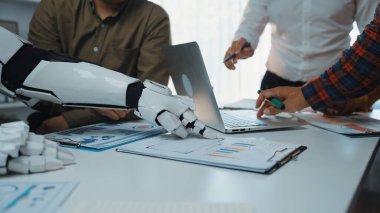 Modern bir ofis ortamında insan eli ve robotik kolun etkileşime girdiği ortak bir toplantı düzenlenir. Bu sahne iş dünyasındaki teknoloji entegrasyonunu vurgular. Noogenesis