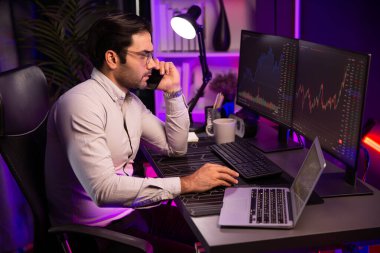 Tüccar akıllı işadamı komisyoncuyu ya da ortağını arıyor, modern evde kârlı bir finans teknolojisi olan neon aydınlatma ofisindeki bilgisayardaki dinamik borsa yatırımlarını analiz ediyor. Tahmin et..