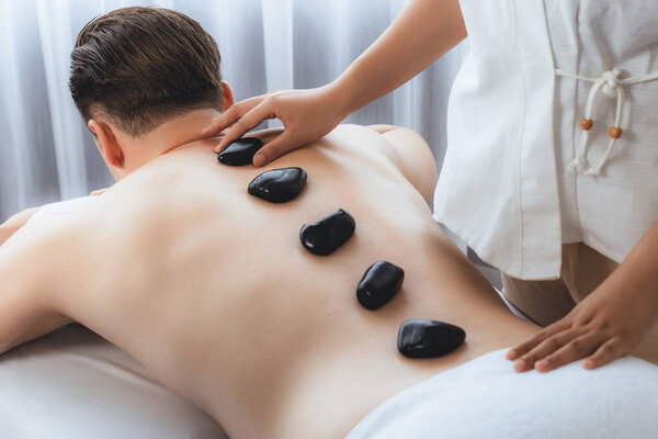 Массаж горячими камнями в спа-салоне на роскошном курорте с дневной легкой атмосферой спокойствия, блаженный клиент, наслаждающийся спа-массажем из базальтового камня скользит по телу с успокаивающим теплом. Quiescent