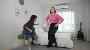 Yatak odasında Asyalı kızıyla müzik eşliğinde dans eden mutlu çekici anne. Beyaz anne dans eder ya da egzersiz yapar. Bu arada tatlı çocuk da müzik eşliğinde yatağa atlar. Aile eğlence konsepti. Pedagoji.