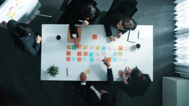 Profesyonel iş adamlarının zaman aşımı pazarlama planını açıklarken beyaz tahtaya yapışkan bir not bırakıyor. Yetenekli çeşitli iş gruplarının yukarıdan görünüşü beyin fırtınası stratejisini tartışıyor. Müdürlük.