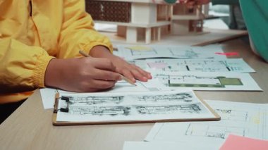 Canlı bir sahne, ayrıntılı planlar ve renkli yapışkan notlarla mimari planlar üzerinde işbirliği yapan profesyonelleri, dinamik bir çalışma ortamı sergileyerek yakalıyor. SACTR