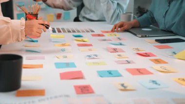 Renkli yapışkan notlar kullanarak fikirler üzerinde işbirliği yapan, modern ofis ortamında yaratıcılığı ve takım çalışmasını teşvik eden çeşitli meslektaşları içeren canlı ve dinamik bir beyin fırtınası oturumu. SACTR