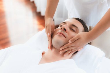 Beyaz adam stres önleyici kafa masajından ve lüks bir tatil beldesi veya otel spa salonundaki modern ışık ortamında yüz güzelliği eğlencelerini şımartmaktan hoşlanıyor. Sessiz.