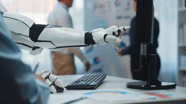 Robotik bir kol modern bir ofiste bir bilgisayara doğru uzanıyor, bir iş görüşmesi sırasında teknoloji ve insan işbirliğini gösteriyor. Noogenesis