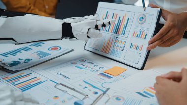 Bir insan ve bir robot çeşitli grafik ve grafiklerle çevrili veri analizinde işbirliği yapıyorlar. Modern teknolojilerin iş karar verme süreçlerindeki rolünü vurgulamak. Noogenesis