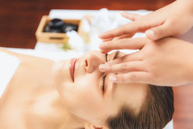 Yakın plan kadın stres önleyici kafa masajı yapmaktan ve lüks tatil beldesi veya otel spa salonundaki modern ışık ortamında yüz güzelliği eğlencelerini şımartmaktan zevk alıyor. Sessiz.