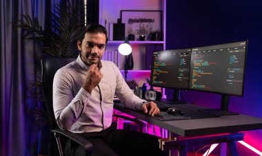 Bilgisayar ekranındaki yazılım geliştirme kodlamasına karşı poz vermek için akıllı bilişim geliştirici görünümlü kamera profilleri, neon ışıklı siber oda ofisinde program güncellemesi internet sitesi verileri sunuyor. Tahmin et..