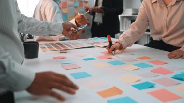 Çeşitli profesyonellerden oluşan bir grup, canlı bir ofis toplantısında yenilikçi fikirler üretmek için masaya renkli yapışkan notlar kullanarak dinamik beyin fırtınası yapıyor. SACTR