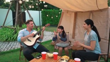 Baba gitar çalarken anne ve kız birlikte kampta oturuyorlar. Ebeveynler, genç nesil çapraz kuşak farklılıklarıyla zaman geçirmek için açık hava kamp aktivitelerini kullanıyorlar. Uyumsuzluk.