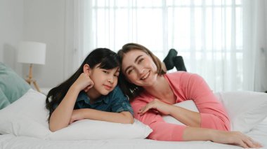 Mutlu Asyalı kız ve akıllı anne kameraya bakarken yatağa uzanıyorlar. Enerjik aile vakit geçirir ve birlikte yatmaya hazırlanır. Sevimli kız ve anne kameraya gülümsüyor sevgi ve şefkat gösteriyorlar. Pedagoji.