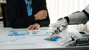 Bir insan ve robot elin veri analizinde işbirliği yaptığı modern bir ofis sahnesi. İş görüşlerini vurgulayan grafikler ve grafiklerle raporlara odaklan. Noogenesis