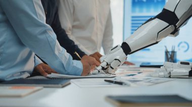 Yenilikçi takım çalışmalarının geleceğini yansıtan belgeler üzerinde insan eli ve robot kolunun birlikte çalıştığı modern bir ofiste ilgi çekici bir işbirliği sahnesi. Noogenesis