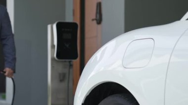 İlerici adam evindeki elektrikli aracın aküsüne emisyonsuz güç bağlantısı kuruyor. Elektrikli araç elektrik istasyonundan EV araba aküsüne kabloyla şarj oluyor.