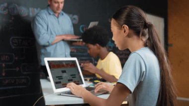 Afrikalı erkek manken tamir ederken beyaz kız programlama ya da kodlama sistemi. Öğretmen elinde dizüstü bilgisayar tutarken çeşitli çocukların web geliştirme programı yazmalarına bakıyor. Yenilik eğitimi. Öğretim