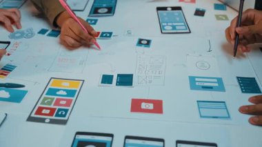 Çeşitli ellerin mobil ve web uygulamaları için kullanıcı arayüzleri tasarlamakla aktif olarak ilgilenen yakın plan görüntüsü, kağıt üzerinde işbirlikçi bir beyin fırtınası oturumu sergiliyor. SACTR