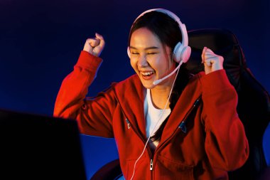 Yüzünde kulaklık renginde kulaklık takan, neon odada online oyun oynayan, Esport meziyetli takım oyuncularına yumruk kaldırarak oynayan güzel Asyalı kız flamasının sunucu kanalı. Taktik.