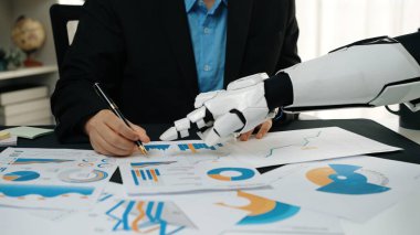 Bir insan, üretkenliği artırmak ve gelecek için yenilikçi çözümler bulmak için bir ofiste robot eliyle birlikte çeşitli grafik ve grafikleri analiz eder. Noogenesis