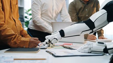 Fütüristik bir sahne, günümüz çalışma ortamında teknoloji ve takım çalışmasının entegrasyonunu temsil eden modern bir ofiste robot kolla etkileşen bir insanı gösteriyor. Noogenesis