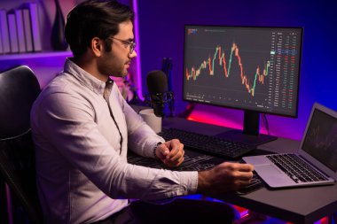 Akıllı tüccar işadamı, karanlık oda gecesinde neon ışıklı ofisteki arama pazarında yüksek kârla ekranda bilgisayar ve bilgisayar üzerinde dinamik borsa yatırımları üzerinde yoğunlaşıyor. Tahmin et..