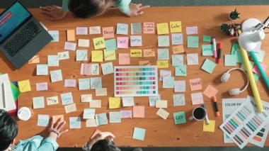 Sıradan giyinen, dizüstü bilgisayara bakan ve fikir paylaşan iş adamlarının en aşağıdan görünüşü. Yapışkan notlar ve kulaklıkla masada çalışan ve renk paletini kontrol eden yöneticinin hava görüntüsü. Sempozyum.