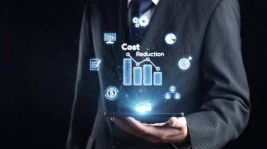 Resmi takım elbiseli bir işadamı, maliyet azaltma stratejilerini temsil eden, modern finansal analizler ve yenilikleri gösteren parlak çizelgeler ve grafikler içeren bir tablet tutuyor. Dörtgen