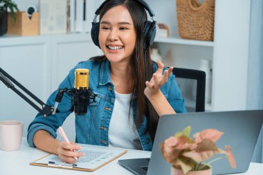 Sosyal medyada kulaklıkla canlı yayın yapan Asyalı sunucu modern stüdyoda yaşam koçluğu veya pazarlama dinleyicilerini selamlıyor. Taktik.