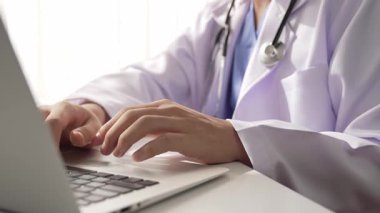 Hastanedeki doktor masasında oturup dizüstü bilgisayar üzerinde çalışıyor. Hasta test sonuçlarını teşhis ediyor, hastalıklar ve hastalıklar için tedavi planı geliştiriyor. Sağlık personeli ve sağlık hizmetleri. Ağır çekim. Katı.