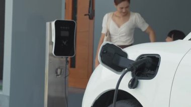İlerici ebeveynler kızlarını okuldan alırken elektrikli araba ve yenilenebilir enerji kavramını kullandılar, evdeki EV otomobil için şarj istasyonu. Alternatif eko taşımacılığı.