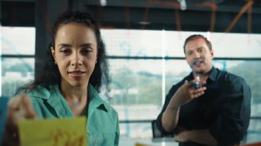 Profesyonel iş adamları yaratıcı pazarlama fikrini modern ofiste tartışırlar. İş adamları cam tahtada yapışkan notlar kullanarak finansal plan üzerinde çalışıyor. Yönlendirici.