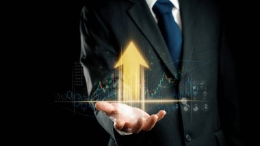 Bir iş adamı, dijital bir grafik ve bir okun yer aldığı yukarı doğru büyümenin kendine güvenen bir görüntüsünü sunuyor. Karanlık arka plan finansal başarıya olan bağlılığı vurguluyor. Dörtgen