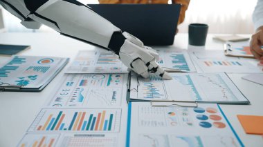 Robotik bir el modern bir ofiste çeşitli iş veri tabloları ile etkileşime girer, çağdaş bir çalışma alanında teknoloji ve analizin birleşmesini gösterir. Noogenesis