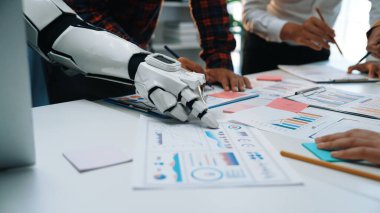 Bir robot kol modern bir ofis masasında insan işçilerle işbirliği yapar, veri analizi, grafik sunumları ve stratejik planlama faaliyetleri ile ilgilenir.