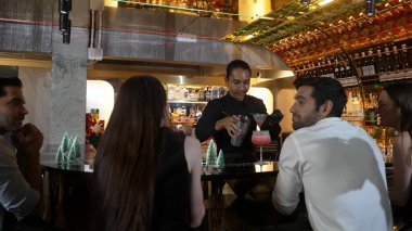 Gülümseyen Asyalı barmen VIP konuğuyla konuşurken süslü Noel ağacı tezgahında karışık kokteyl hazırlıyor. Gece kulübü lüksünde gece hayatını gösteren özel bir içecek. Vinosity.