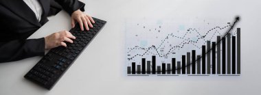 Bir iş adamı, klavye kullanarak ve başarı gösteren bir büyüme eğilimi tablosu izleyerek, modern bir çalışma alanında finansal veri analizine odaklanmaktadır. Etki