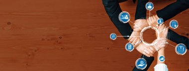 Çeşitli bir iş ekibi, çeşitli alanları ve kavramları temsil eden dijital simgelerle çevrili bir çember oluşturan ellerle sembolize edilen ortak strateji oturumuna girişir. Dostluk