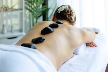 Lüks tatil köyündeki kaplıcalarda sıcak taş masajı. Gün ışığı sükunet ortamında, mutlu kadın müşteri bazalt taş masajından zevk alıyor. Rahatlatıcı bir sıcaklıkla vücudun üzerinde süzülüyor. Sessiz.