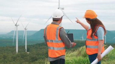 Erkek ve kadın mühendisler kırsal kesimdeki bir tepenin tepesinde ya da dağda rüzgar çiftliğinde çalışıyorlar. Yenilenebilir ve sürdürülebilir enerjinin gelecekteki üretimi için yenilikçi idealler.