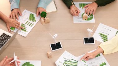 Eko evi projesini yel değirmeni tasarım modeli ve karbon ayak izini azaltmak için yeşil enerji kullanım grafiği ile toplantı masasında tartışan harika bir iş ekibi. Dünyayı kurtarın. Eline odaklan. Tanımlama.