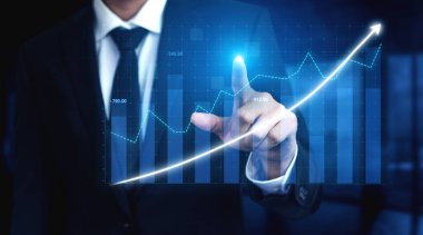Bir işadamı büyüme eğilimlerini vurgulayan dijital bir grafikle etkileşime girer. Modern ofis geçmişi yenilikçiliğe ve stratejik başarıya olan bağlılığı yansıtır. Etki